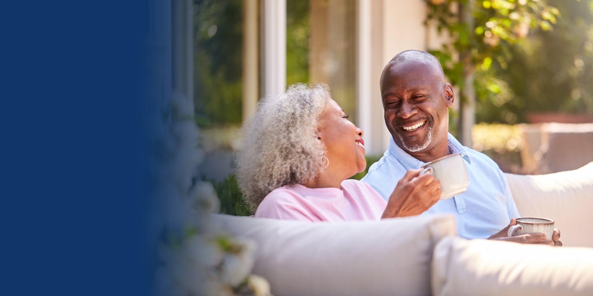 Older couple sitting outside on a couch enjoying cups of tea