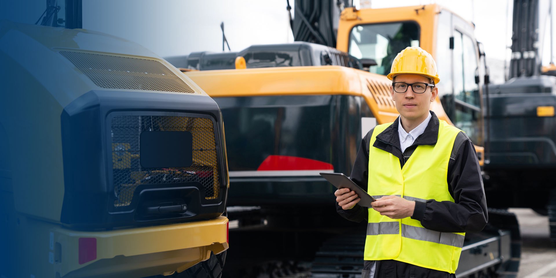 Man in a suit and hardhat holding a clipboard in front of construction equipment.