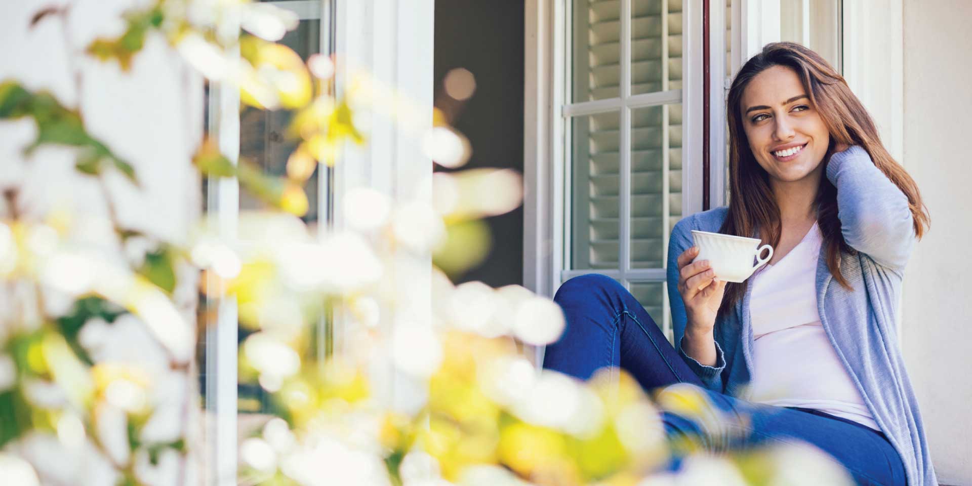 A woman sitting on her window sill sipping coffee