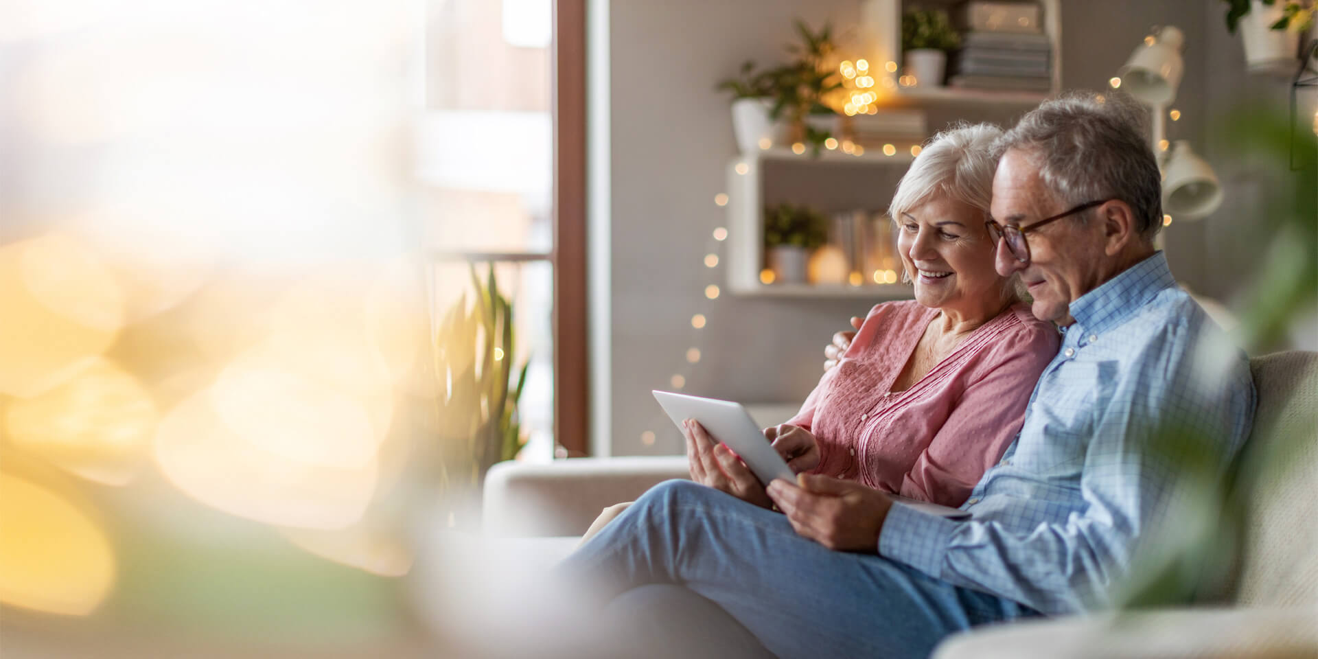 An older couple sitting on the couch looking at their tablet